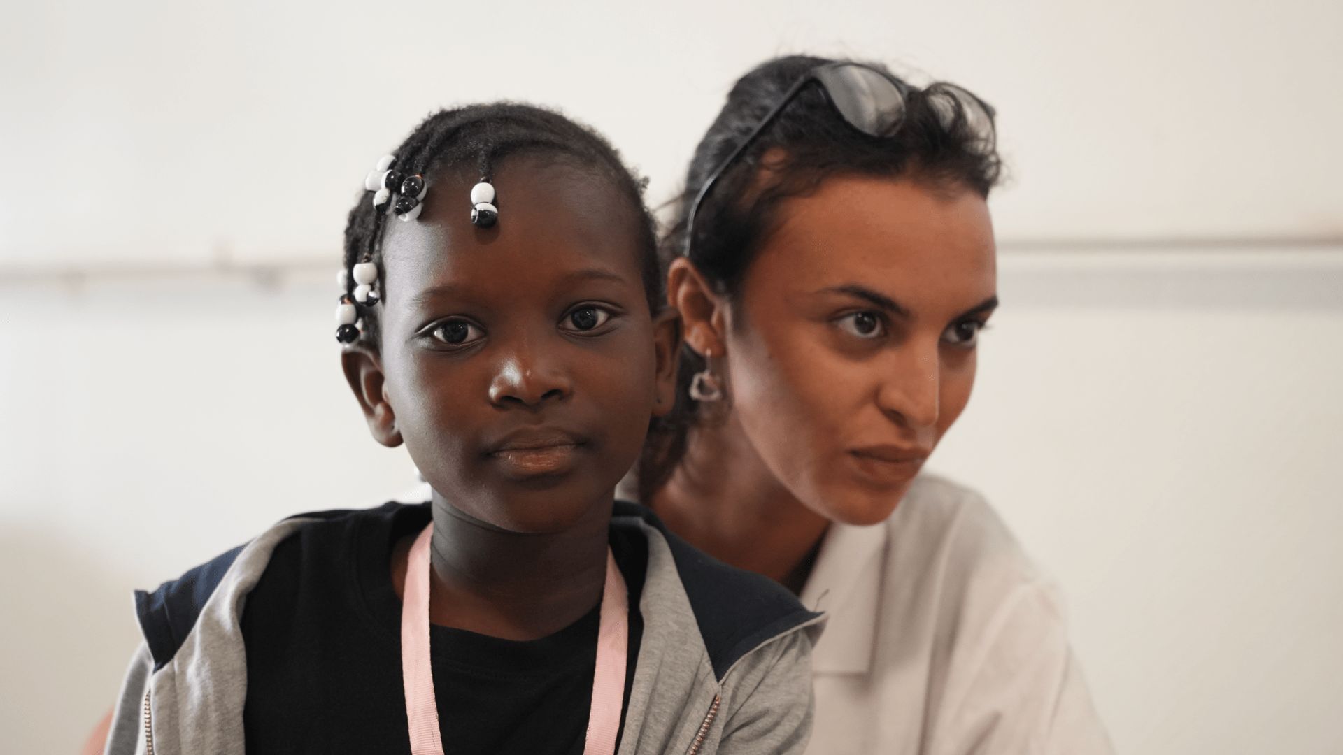 Fillette avec tresses à perles accompagnée d'une professionnelle de santé en blouse blanche.