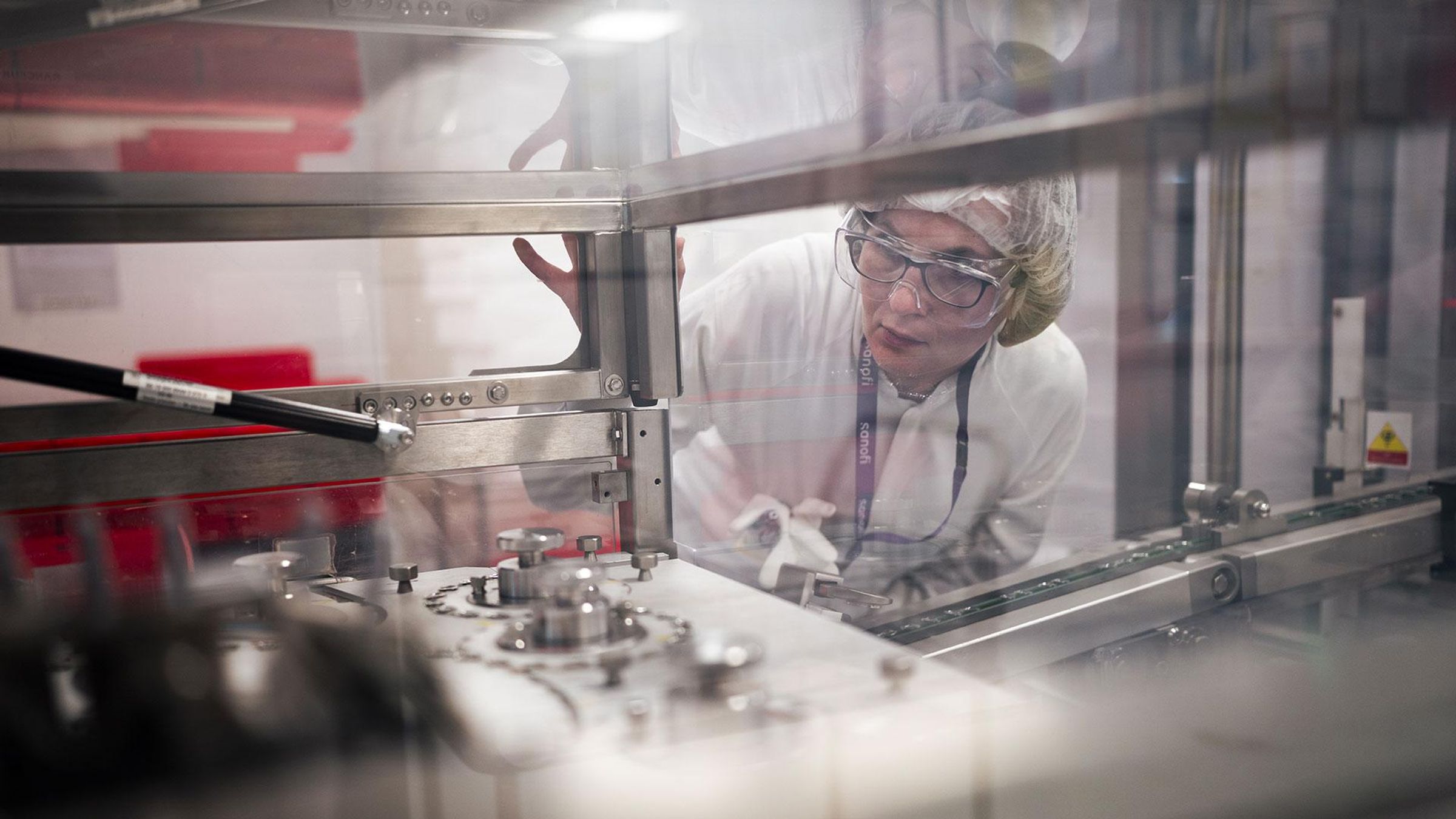 Nadège en tenue de laboratoire inspectant un équipement de production à travers une vitre.