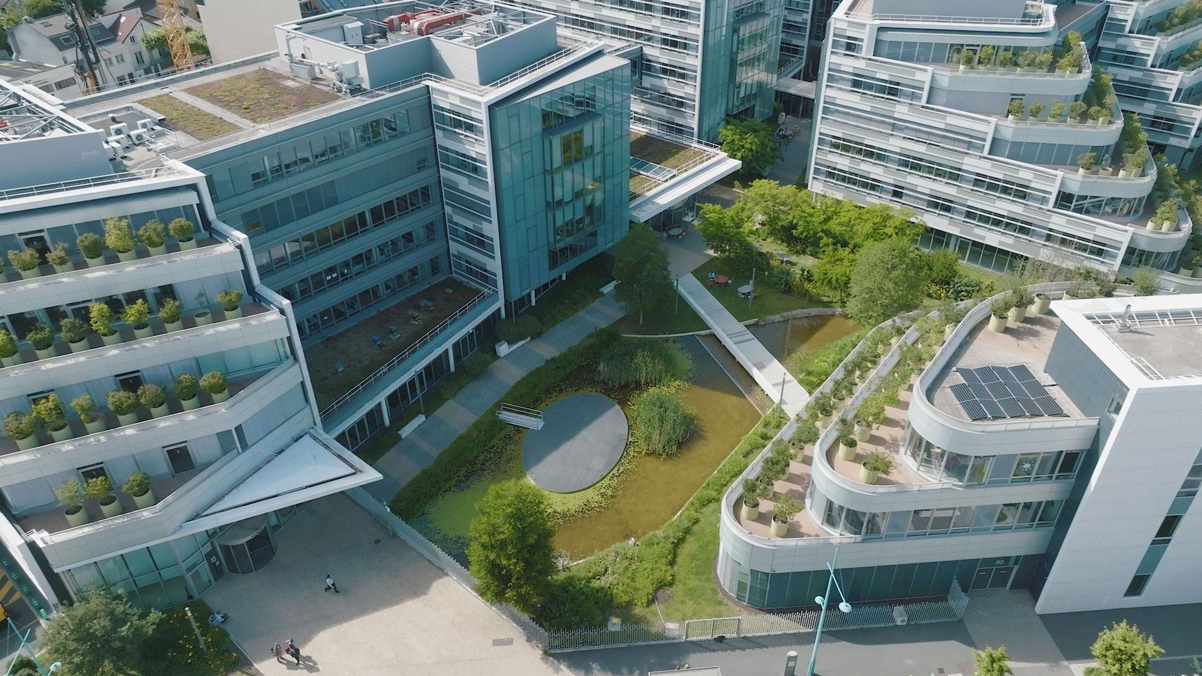 Vue aérienne d’un campus avec bâtiments modernes, espaces verts et plan d'eau.
