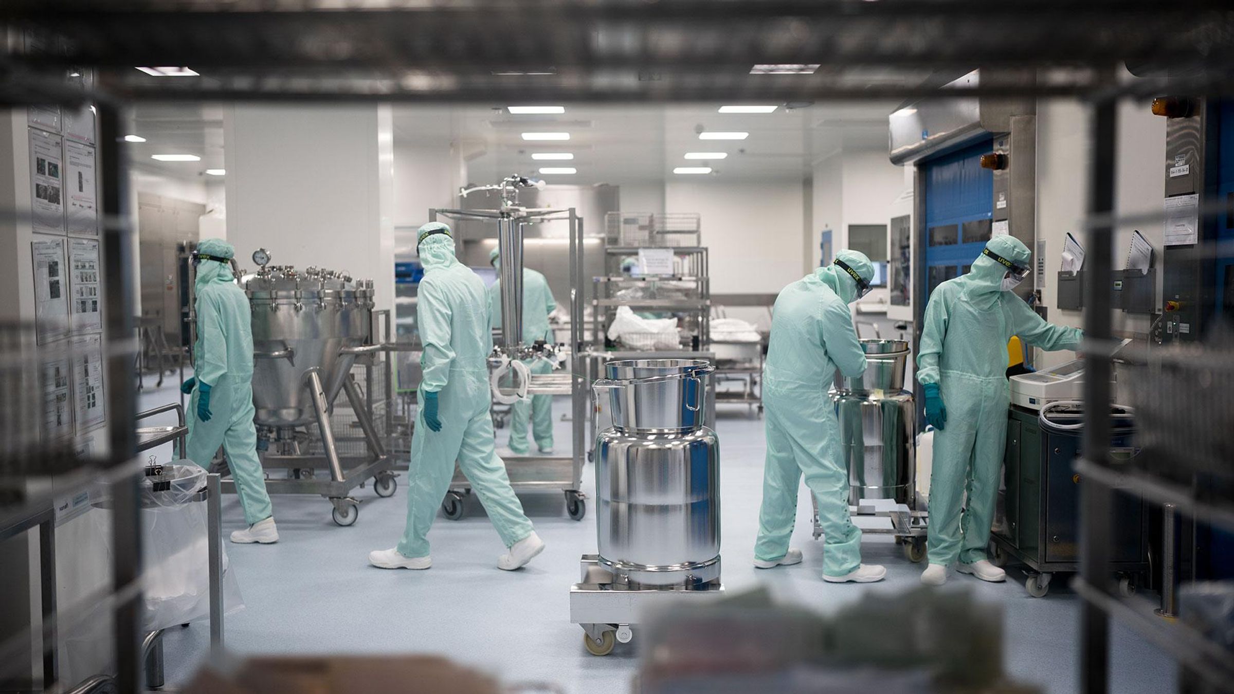 Équipe de cinq opérateurs en tenue de salle blanche travaillant avec des équipements de production pharmaceutique.