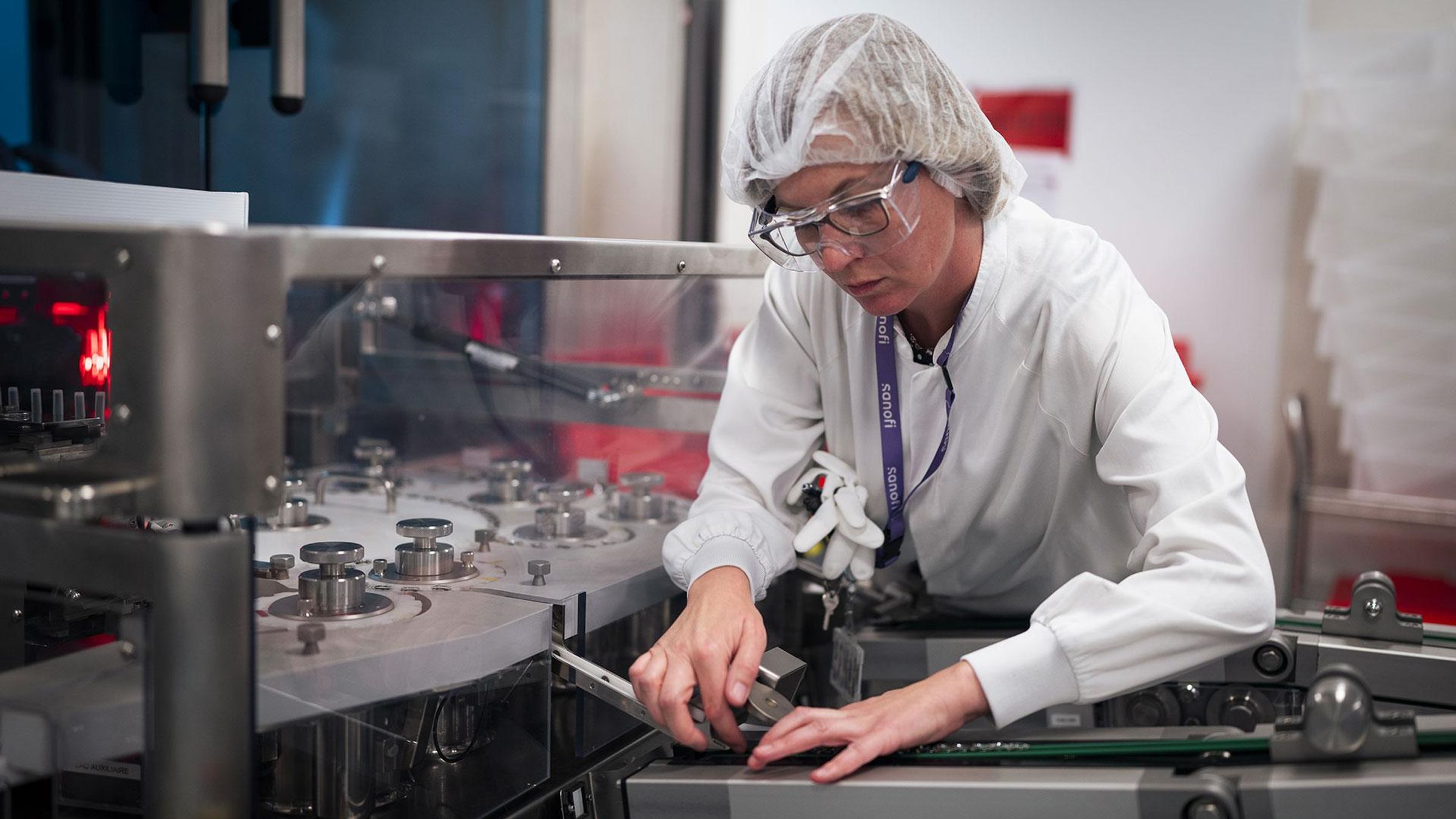 Femme en charlotte et blouse ajustant un équipement de laboratoire.