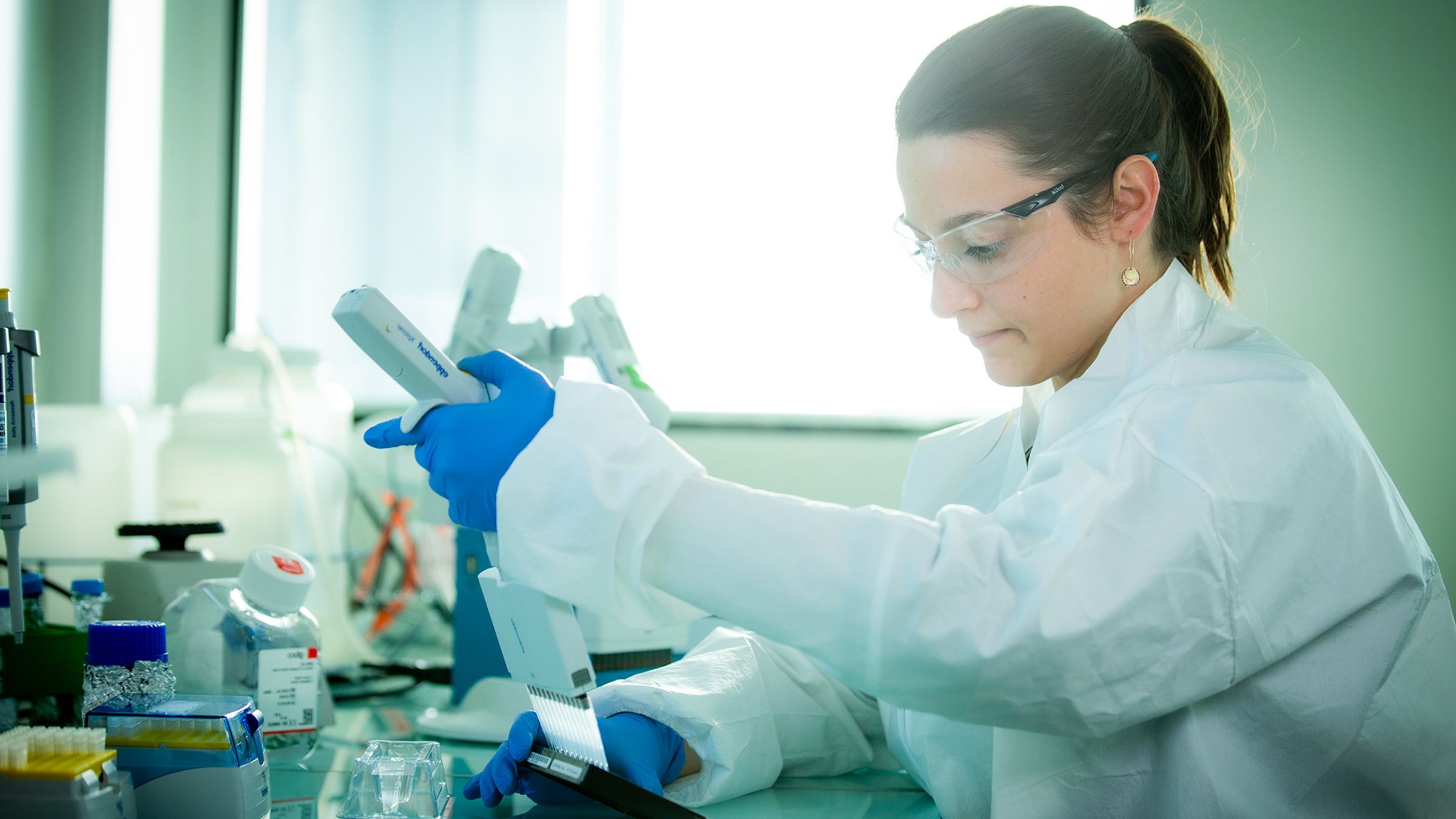 Chercheuse en tenue de laboratoire manipulant une pipette avec des tubes à essai, en laboratoire.