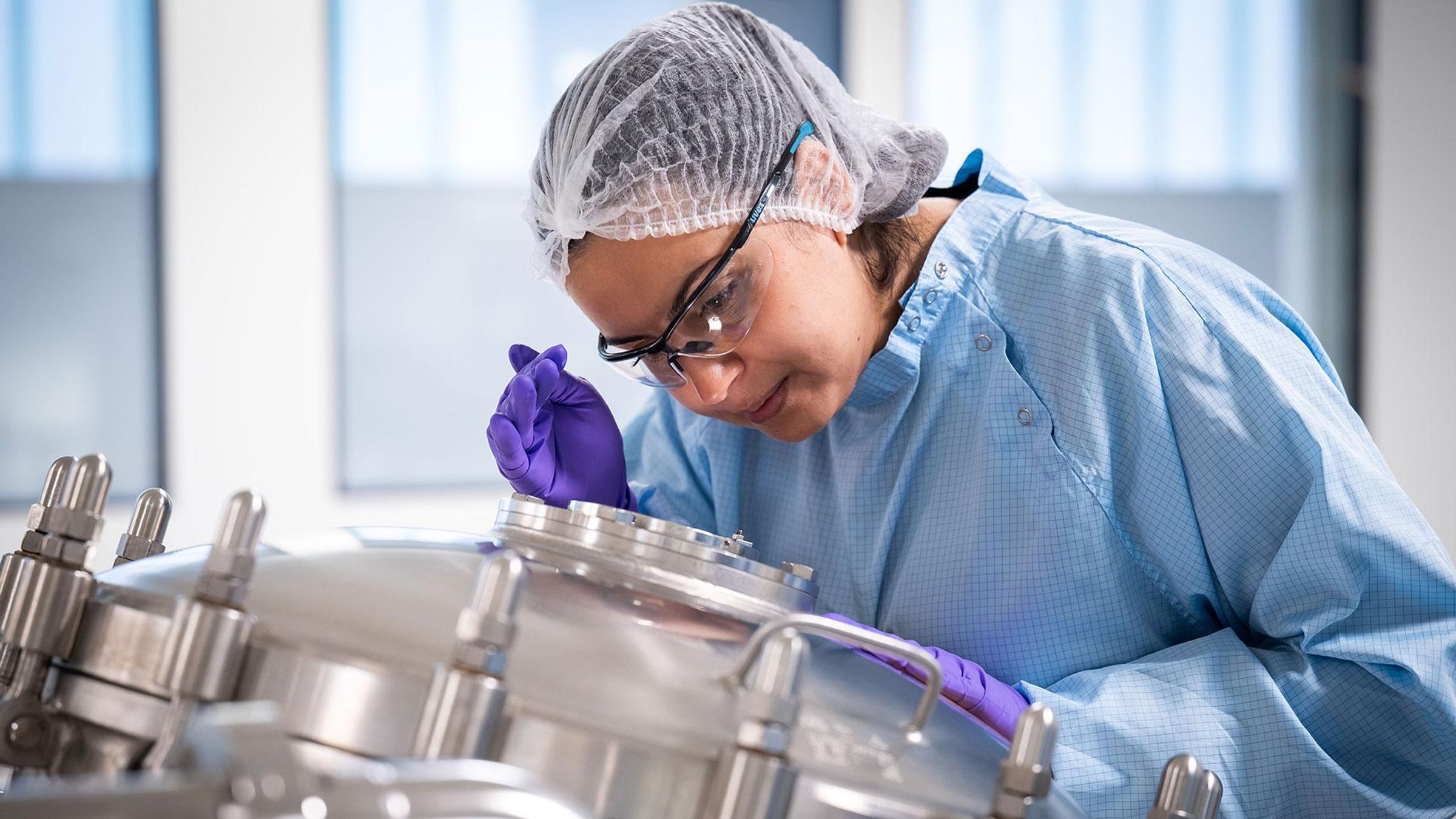 Samia, en combinaison bleue et gants violets inspectant un bioréacteur.