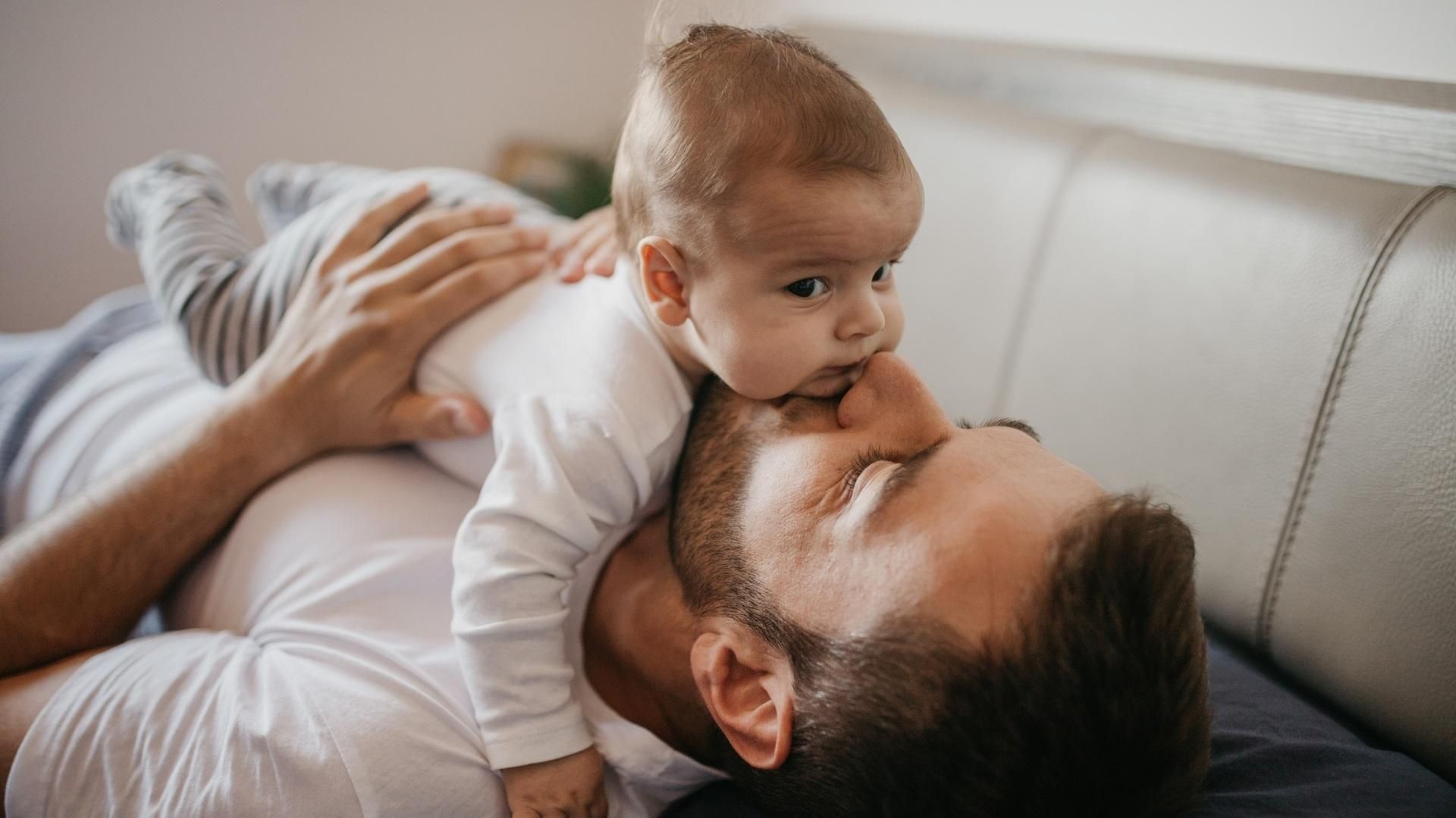 Père allongé sur un canapé tenant tendrement son bébé sur sa poitrine dans un moment de complicité.