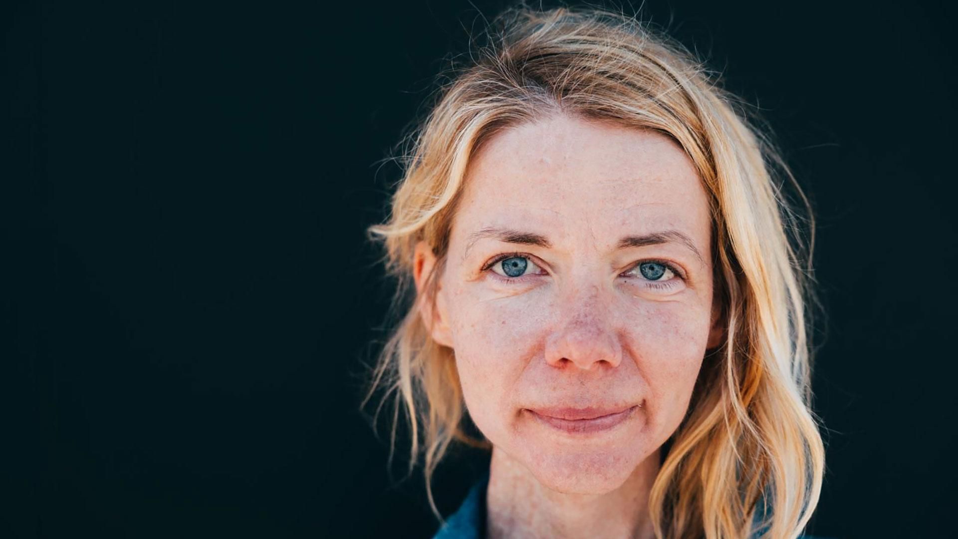 : Céline aux cheveux blonds courts et yeux bleus, avec un léger sourire, portrait sur fond sombre